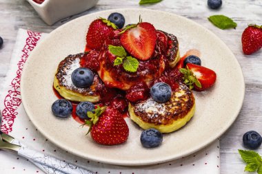 Taze böğürtlen ve çilek soslu süzme peynirli krep. Sağlıklı kahvaltı konsepti. Olgun yaban mersini, kokulu nane yaprakları, çatal bıçak takımı. Tahta kaplama arka plan, kapat