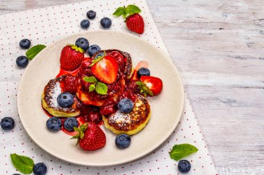 Taze böğürtlen ve çilek soslu süzme peynirli krep. Sağlıklı kahvaltı konsepti. Olgun yaban mersini, mis kokulu nane yaprakları. Tahta kaplama arka plan, kopyalama alanı