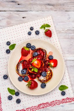 Taze böğürtlen ve çilek soslu süzme peynirli krep. Sağlıklı kahvaltı konsepti. Olgun yaban mersini, mis kokulu nane yaprakları. Tahta kaplama arka plan, üst görünüm