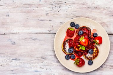 Taze böğürtlen ve çilek soslu süzme peynirli krep. Sağlıklı kahvaltı konsepti. Olgun yaban mersini, mis kokulu nane yaprakları. Tahta kaplama arka plan, üst görünüm