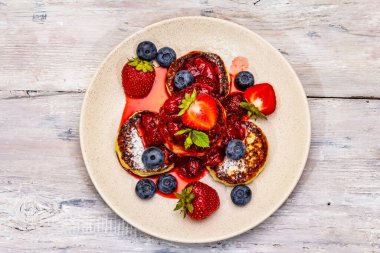 Taze böğürtlen ve çilek soslu süzme peynirli krep. Sağlıklı kahvaltı konsepti. Olgun yaban mersini, mis kokulu nane yaprakları. Tahta kaplama arka plan, üst görünüm