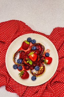 Taze böğürtlen ve çilek soslu süzme peynirli krep. Sağlıklı kahvaltı konsepti. Olgun yaban mersini, mis kokulu nane yaprakları, kırmızı benekli peçete. Taş beton zemin, üst görünüm