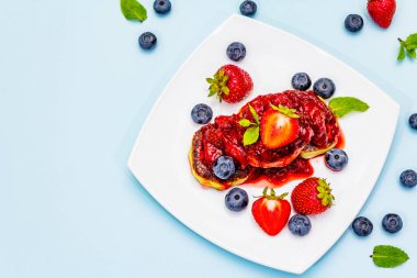 Taze böğürtlen ve çilek soslu süzme peynirli krep. Çocuklar için sağlıklı ve komik kahvaltı konsepti. Olgun yaban mersini, mis kokulu nane yaprakları. Yumuşak mavi arkaplan, üst görünüm