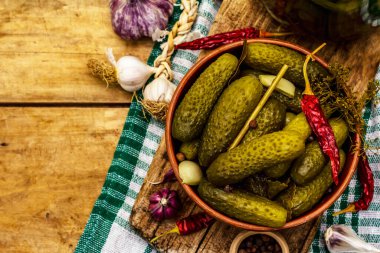 Baharat ve bitkilerle marine edilmiş salatalık turşusu. Geleneksel ev yapımı fermente aperatifler kil kasede. Eski ahşap masa, üst manzara.