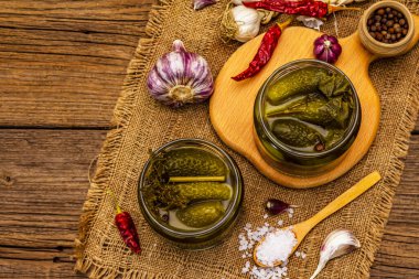 Baharat ve bitkilerle marine edilmiş salatalık turşusu. Cam kavanozlarda geleneksel ev yapımı fermente aperatif. Eski tahta kaplama arka plan, üst görünüm
