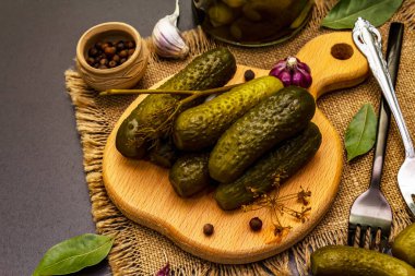 Baharat ve bitkilerle marine edilmiş salatalık turşusu. Geleneksel Doğu Avrupa aperatifleri cam kavanozlarda ve tahta kesme tahtalarında. Moda siyah taş beton arka plan, kapat