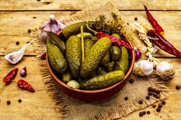 Baharat ve bitkilerle marine edilmiş salatalık turşusu. Geleneksel ev yapımı fermente aperatifler kil kasede. Eski ahşap masa, kapat.