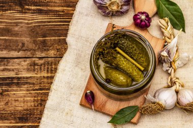 Baharat ve bitkilerle marine edilmiş salatalık turşusu. Geleneksel fermente aperatifler cam kavanozda. Tahta kaplama arka plan, üst görünüm