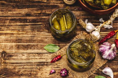 Baharat ve bitkilerle marine edilmiş salatalık turşusu. Geleneksel fermente aperatifler cam kavanozlar ve kil kaselerde. Tahta kaplama arka plan, üst görünüm