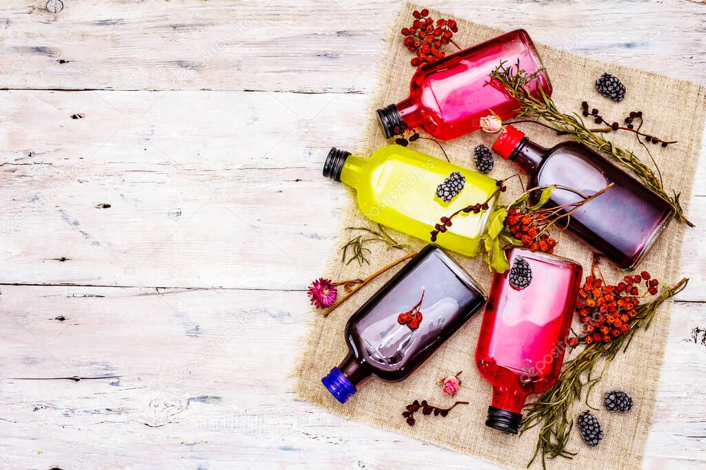 Homemade assortment of berries liqueurs or tincture. Sweet mountain fruits, fragrance herbs, glass bottles. White old wooden boards background, top view