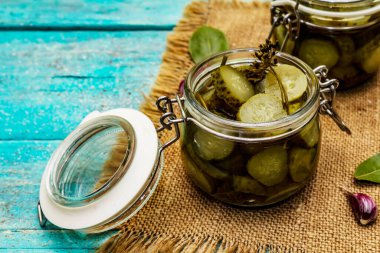 Baharat ve bitkilerle marine edilmiş salatalık turşusu. Geleneksel fermente aperatif cam kavanoz ve seramik kasede. Turkuaz ahşap tahta arka plan, kapat