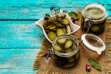 Baharat ve bitkilerle marine edilmiş salatalık turşusu. Geleneksel fermente aperatif cam kavanoz ve seramik kasede. Turkuaz tahta tahtalar arka plan, kopyalama alanı