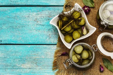 Baharat ve bitkilerle marine edilmiş salatalık turşusu. Geleneksel fermente aperatif cam kavanoz ve seramik kasede. Turkuaz ahşap tahta arka plan, üst görünüm