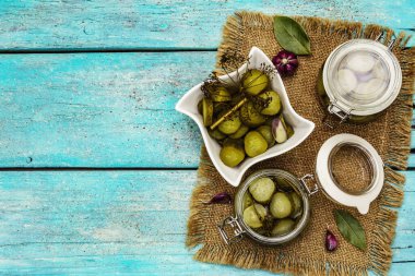 Baharat ve bitkilerle marine edilmiş salatalık turşusu. Geleneksel fermente aperatif cam kavanoz ve seramik kasede. Turkuaz ahşap tahta arka plan, üst görünüm