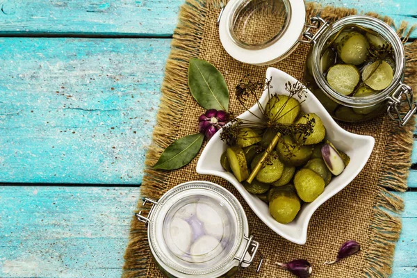 Baharat ve bitkilerle marine edilmiş salatalık turşusu. Geleneksel fermente aperatif cam kavanoz ve seramik kasede. Turkuaz ahşap tahta arka plan, üst görünüm