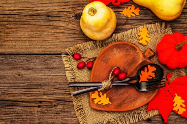 Sonbahar sofrası. Şükran Günü ya da Cadılar Bayramı. Yaprak şeklinde seramik tabak, siyah çatal bıçak takımı, balkabağı ve köpek gülü böğürtlenleri. Eski tahta arka plan, üst görünüm
