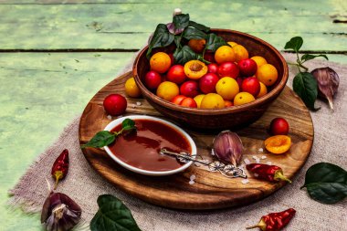 Sarımsaklı ve acı biberli Tkemali Gürcü kiraz sosu. Olgun meyve ve baharatlardan geleneksel sos. Yumuşak yeşil ahşap arka plan, kapat