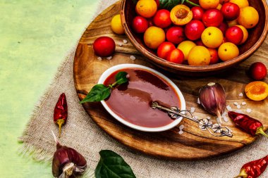 Sarımsaklı ve acı biberli Tkemali Gürcü kiraz sosu. Olgun meyve ve baharatlardan geleneksel sos. Yumuşak yeşil ahşap arka plan, kapat