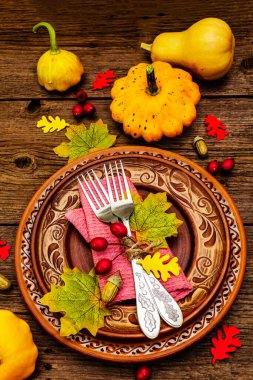Sonbahar ve Şükran Günü yemeği. Balkabağı ve böğürtlen hasadı renkli yapraklar, seramik tabaklar, çatallar ve peçete. Çatal bıçak takımı ahşap arka plan, üst görünüm