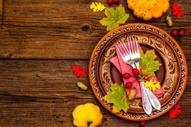 Sonbahar ve Şükran Günü yemeği. Balkabağı ve böğürtlen hasadı renkli yapraklar, seramik tabaklar, çatallar ve peçete. Çatal bıçak takımı ahşap arka plan, üst görünüm