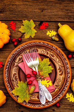 Sonbahar ve Şükran Günü yemeği. Balkabağı ve böğürtlen hasadı renkli yapraklar, seramik tabaklar, çatallar ve peçete. Çatal bıçak takımı ahşap arka plan, üst görünüm