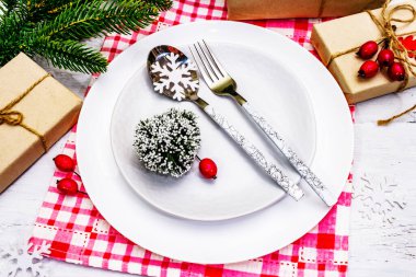 Noel ya da Yeni Yıl Atık Akşam Yemeği Yeri. Seramik tabaklar, hediye, kar taneleri, yaban mersini ve tematik dekor. Beyaz tahta arka planda şenlikli çatal bıçak seti, kapatın.