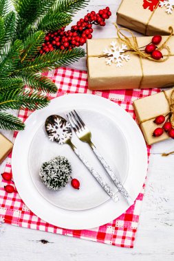 Noel ya da Yeni Yıl Atık Akşam Yemeği Yeri. Seramik tabaklar, hediye, kar taneleri, yaban mersini ve tematik dekor. Beyaz tahta arka planda şenlikli çatal bıçak seti, kapatın.