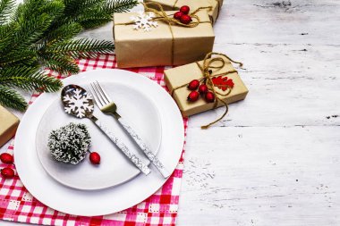 Noel ya da Yeni Yıl Atık Akşam Yemeği Yeri. Seramik tabaklar, hediye, kar taneleri, yaban mersini ve tematik dekor. Beyaz tahta arka planda şenlikli çatal bıçak takımı, kopyalama alanı