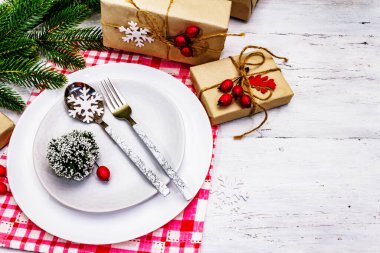 Noel ya da Yeni Yıl Atık Akşam Yemeği Yeri. Seramik tabaklar, hediye, kar taneleri, yaban mersini ve tematik dekor. Beyaz tahta arka planda şenlikli çatal bıçak takımı, kopyalama alanı