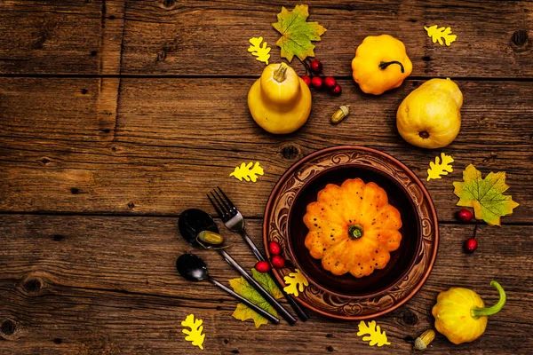 Sonbahar ve Şükran Günü yemeği. Balkabağı ve böğürtlen hasadı, renkli yapraklar, seramik tabak ve kase, çatal, kaşık ve meşe palamudu. Çatal bıçak takımı ahşap arka plan, üst görünüm
