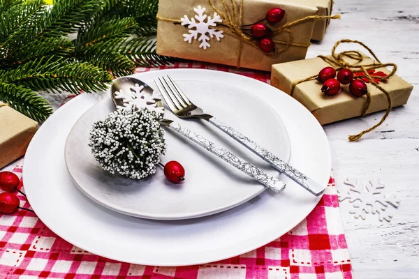 Noel ya da Yeni Yıl Atık Akşam Yemeği Yeri. Seramik tabaklar, hediye, kar taneleri, yaban mersini ve tematik dekor. Beyaz tahta arka planda şenlikli çatal bıçak seti, kapatın.
