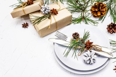 Noel ya da yeni yıl sofrası. Şenlikli çatal bıçak takımı, taze çam dallı seramik tabaklar, koniler, sıfır atık hediye ve yıldız anason. Beyaz macun arkaplanı, kopyalama alanı