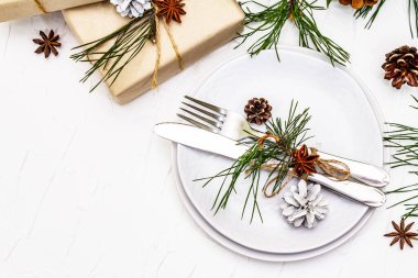 Noel ya da yeni yıl sofrası. Şenlikli çatal bıçak takımı, taze çam dallı seramik tabaklar, koniler, sıfır atık hediye ve yıldız anason. Beyaz macun arkaplan, üst görünüm
