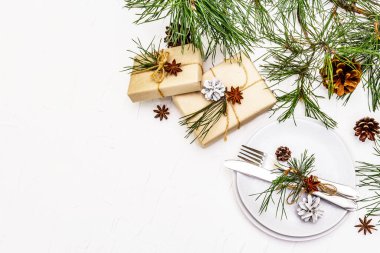 Noel ya da yeni yıl sofrası. Şenlikli çatal bıçak takımı, taze çam dallı seramik tabaklar, koniler, sıfır atık hediye ve yıldız anason. Beyaz macun arkaplan, üst görünüm