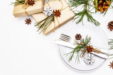 Noel ya da yeni yıl sofrası. Şenlikli çatal bıçak takımı, taze çam dallı seramik tabaklar, koniler, sıfır atık hediye ve yıldız anason. Beyaz macun arkaplan, üst görünüm