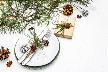 Noel ya da yeni yıl sofrası. Şenlikli çatal bıçak takımı, taze çam dallı seramik tabaklar, koniler, sıfır atık hediye ve yıldız anason. Beyaz macun arkaplanı, kopyalama alanı