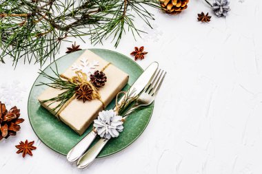 Noel ya da yeni yıl sofrası. Şenlikli çatal bıçak takımı, taze çam dallı seramik tabaklar, koniler, sıfır atık hediye ve yıldız anason. Beyaz macun arkaplanı, kopyalama alanı