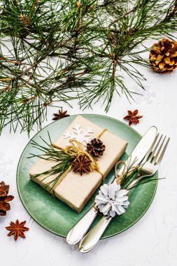 Noel ya da yeni yıl sofrası. Şenlikli çatal bıçak takımı, taze çam dallı seramik tabaklar, koniler, sıfır atık hediye ve yıldız anason. Beyaz macun arkaplanı, kapat