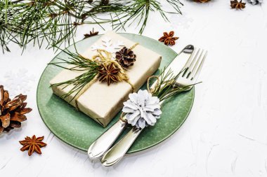 Noel ya da yeni yıl sofrası. Şenlikli çatal bıçak takımı, taze çam dallı seramik tabaklar, koniler, sıfır atık hediye ve yıldız anason. Beyaz macun arkaplanı, kopyalama alanı