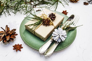 Noel ya da yeni yıl sofrası. Şenlikli çatal bıçak takımı, taze çam dallı seramik tabaklar, koniler, sıfır atık hediye ve yıldız anason. Beyaz macun arkaplanı, kapat