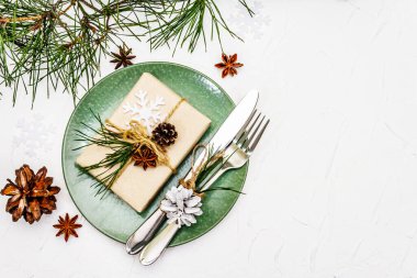 Noel ya da yeni yıl sofrası. Şenlikli çatal bıçak takımı, taze çam dallı seramik tabaklar, koniler, sıfır atık hediye ve yıldız anason. Beyaz macun arkaplan, üst görünüm