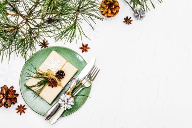 Noel ya da yeni yıl sofrası. Şenlikli çatal bıçak takımı, taze çam dallı seramik tabaklar, koniler, sıfır atık hediye ve yıldız anason. Beyaz macun arkaplan, üst görünüm