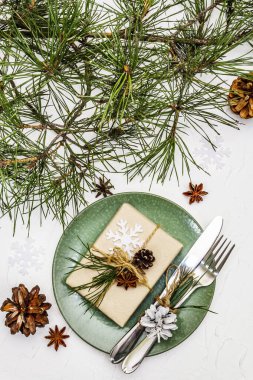Noel ya da yeni yıl sofrası. Şenlikli çatal bıçak takımı, taze çam dallı seramik tabaklar, koniler, sıfır atık hediye ve yıldız anason. Beyaz macun arkaplanı, kapat