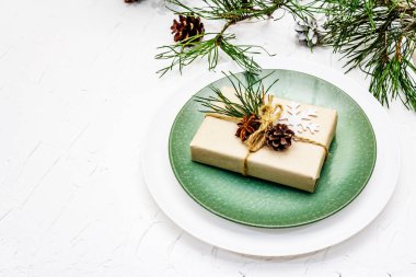 Noel ya da yeni yıl sofrası. Şenlikli çatal bıçak takımı, taze çam dallı seramik tabaklar, koniler, sıfır atık hediye ve yıldız anason. Beyaz macun arkaplanı, kopyalama alanı