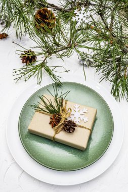 Noel ya da yeni yıl sofrası. Şenlikli çatal bıçak takımı, taze çam dallı seramik tabaklar, koniler, sıfır atık hediye ve yıldız anason. Beyaz macun arkaplanı, kapat
