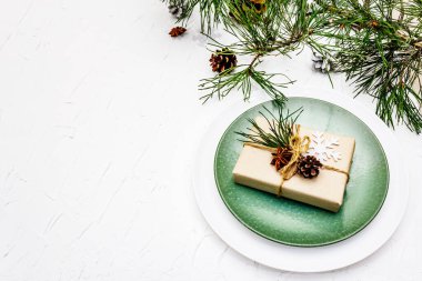 Noel ya da yeni yıl sofrası. Şenlikli çatal bıçak takımı, taze çam dallı seramik tabaklar, koniler, sıfır atık hediye ve yıldız anason. Beyaz macun arkaplan, üst görünüm