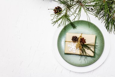 Noel ya da yeni yıl sofrası. Şenlikli çatal bıçak takımı, taze çam dallı seramik tabaklar, koniler, sıfır atık hediye ve yıldız anason. Beyaz macun arkaplan, üst görünüm