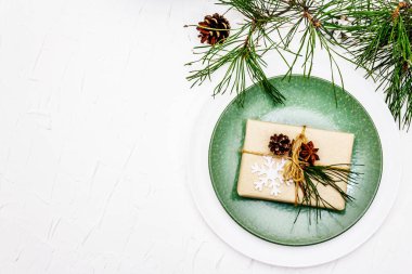 Noel ya da yeni yıl sofrası. Şenlikli çatal bıçak takımı, taze çam dallı seramik tabaklar, koniler, sıfır atık hediye ve yıldız anason. Beyaz macun arkaplan, üst görünüm