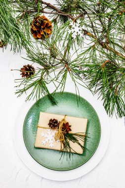 Noel ya da yeni yıl sofrası. Şenlikli çatal bıçak takımı, taze çam dallı seramik tabaklar, koniler, sıfır atık hediye ve yıldız anason. Beyaz macun arkaplanı, kapat