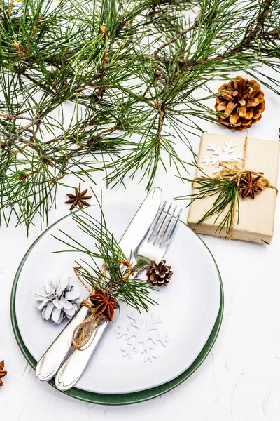 Noel ya da yeni yıl sofrası. Şenlikli çatal bıçak takımı, taze çam dallı seramik tabaklar, koniler, sıfır atık hediye ve yıldız anason. Beyaz macun arkaplanı, kapat